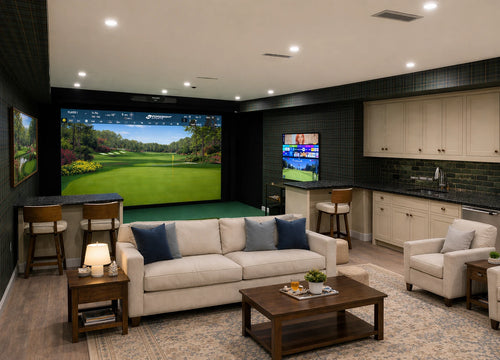 Foresight Falcon golf simulator room with a living room and kitchenette with white couch and stuffed chair and bar sitting facing the screen.