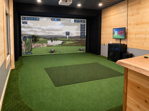 A Custom Foresight GCHawk golf simulator room with a large projection screen showing a golf course, green turf hitting surface, and wood-paneled walls.