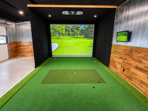 A Foresight Falcon indoor golf simulator setup in a garage with a green turf hitting surface, a large front projection screen showing a golf course, black enclosure walls, wood-paneled side walls, and a 20