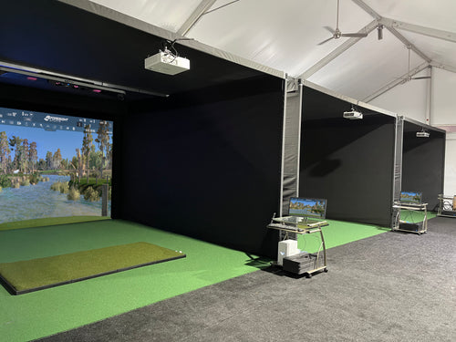 Top-100 golf course, Oakland Hills Country Club temporary winter golf simulator facility inside a tent with multiple screens, and green turf. 