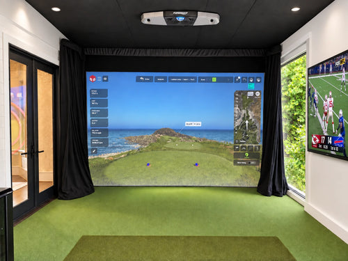 A Foresight Falcon golf simulator installed in an all season patio with a large projection screen showing a golf course simulation, green turf hitting mat in the foreground, black curtains, side windows, and a TV on the right.