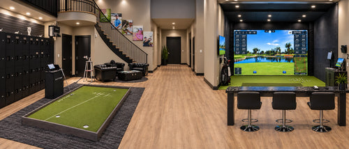 Twenty Scratch golf simulator setup featuring a putt view putting and golf simulator with a green turf target, a black locker room wall, a staircase, and bar stools with granite countertop.