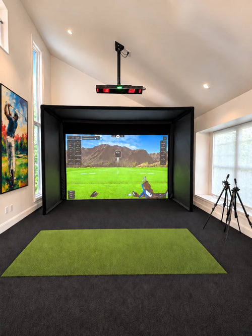 A Uneekor Eye XO2 with Medalist enclosure home golf simulator setup featuring a bright vaulted ceiling family room, a large projected golf course scene on the screen, a black turf, green hitting mat, and two tripods to the right.